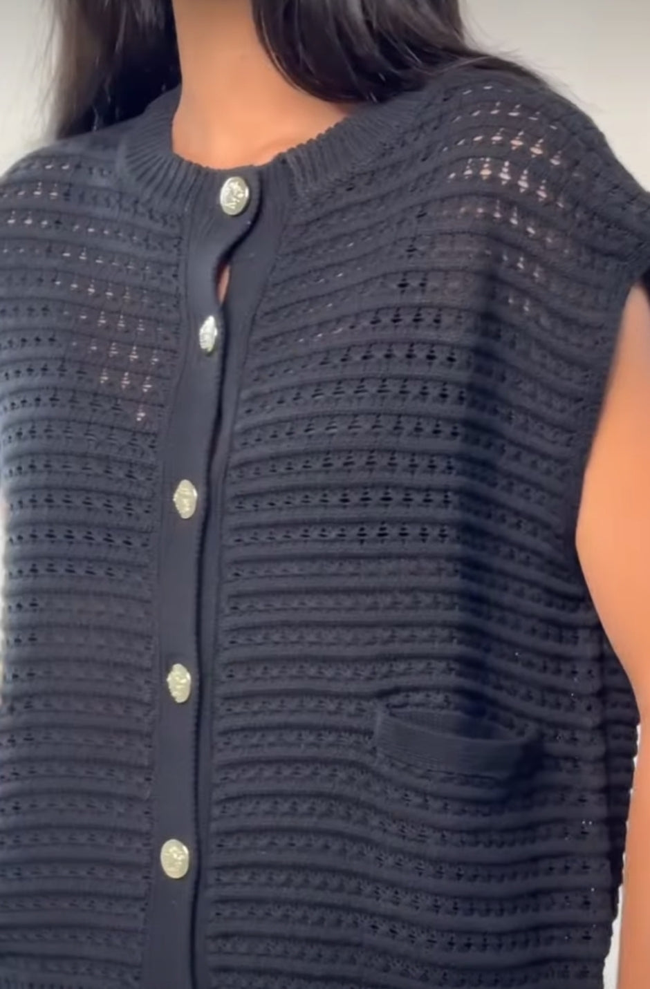 front of a woman wearing a black knit sweater vest with big metal buttons