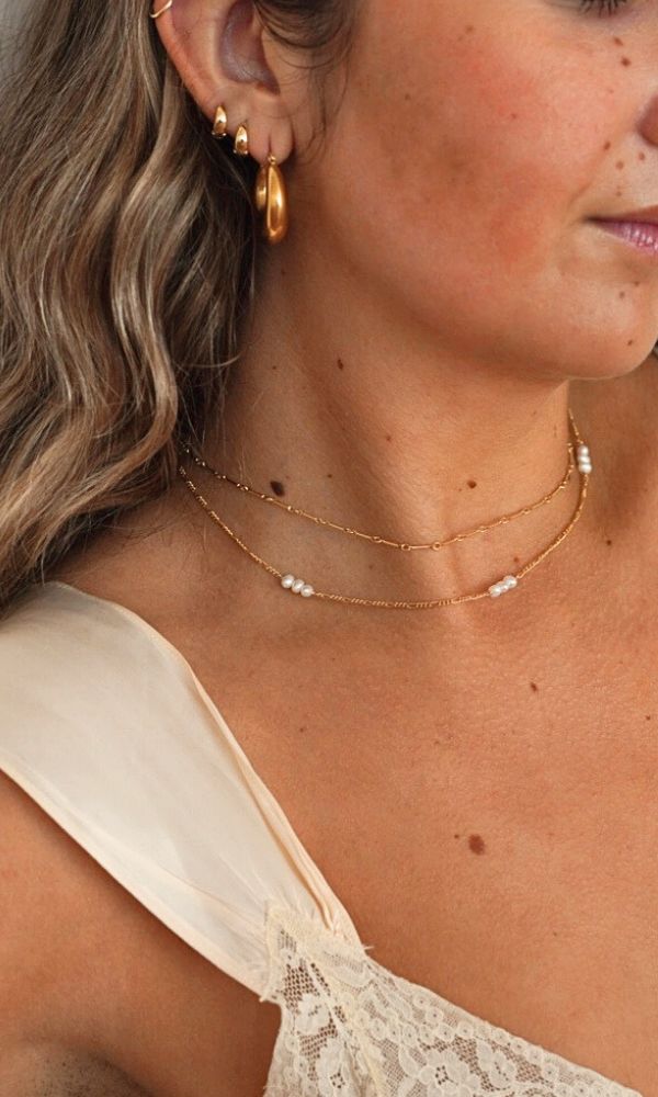 Close-up of a woman wearing gold dainty pearl necklaces and earrings.