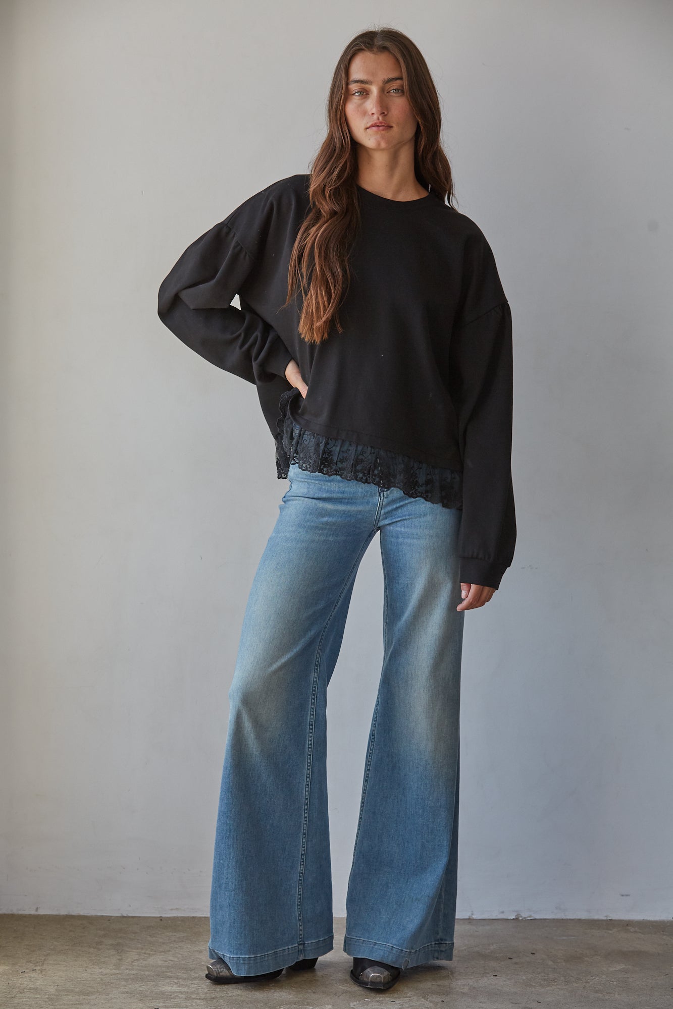 A woman modeling a black long-sleeve crewneck cotton sweatshirt with a lace hem, paired with wide-leg blue jeans.