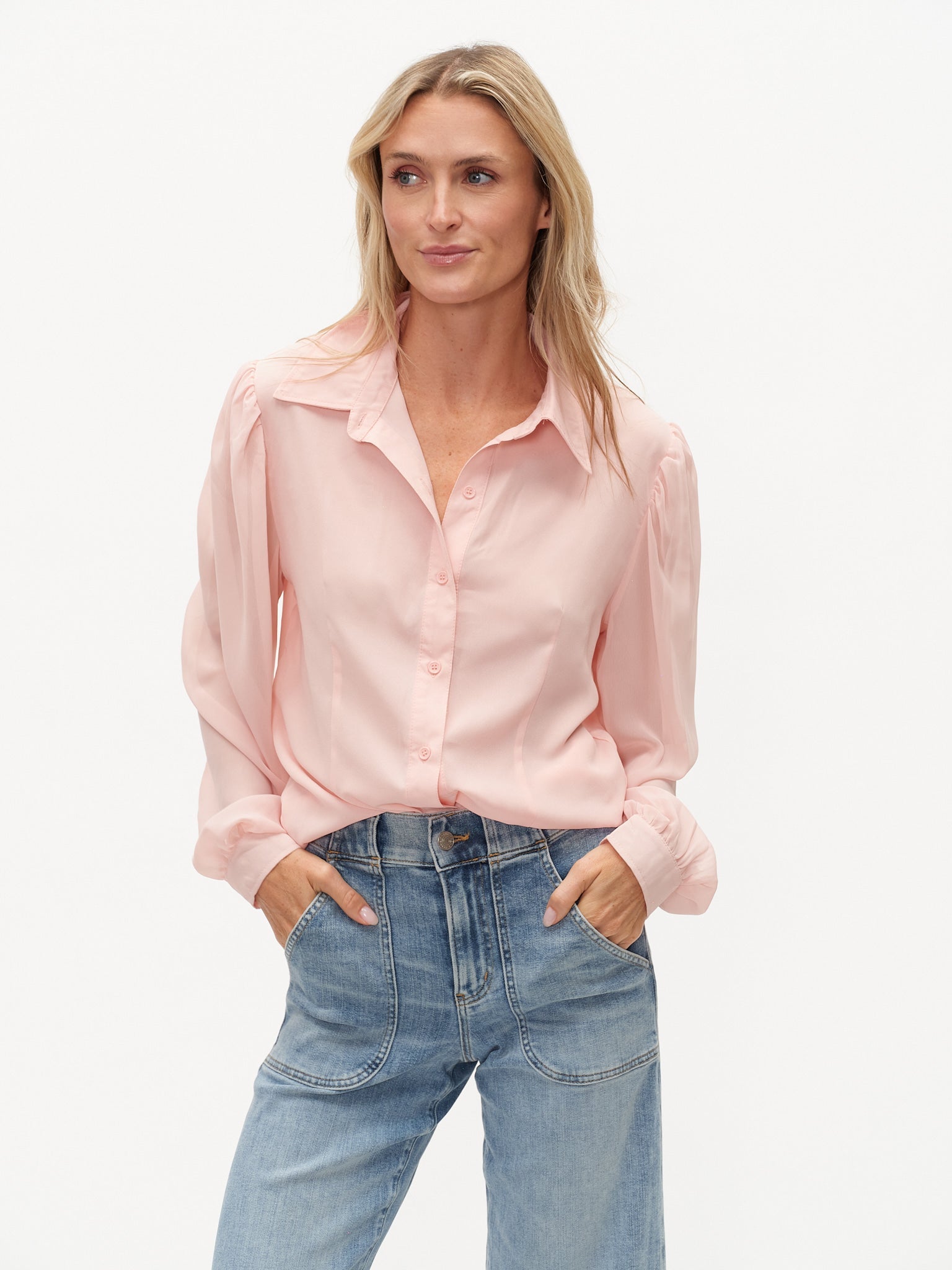 Model wearing a light pink blouse long sheer sleeves and solid knot body.