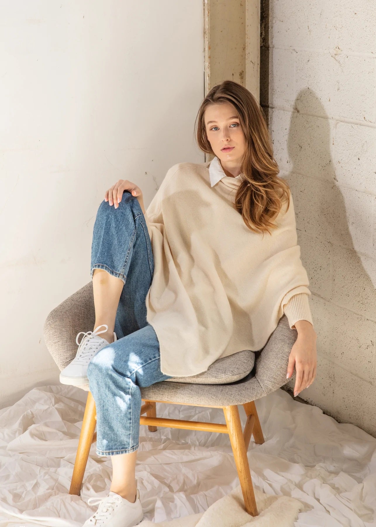 Model sitting in a chair wearing a taupe knit poncho.
