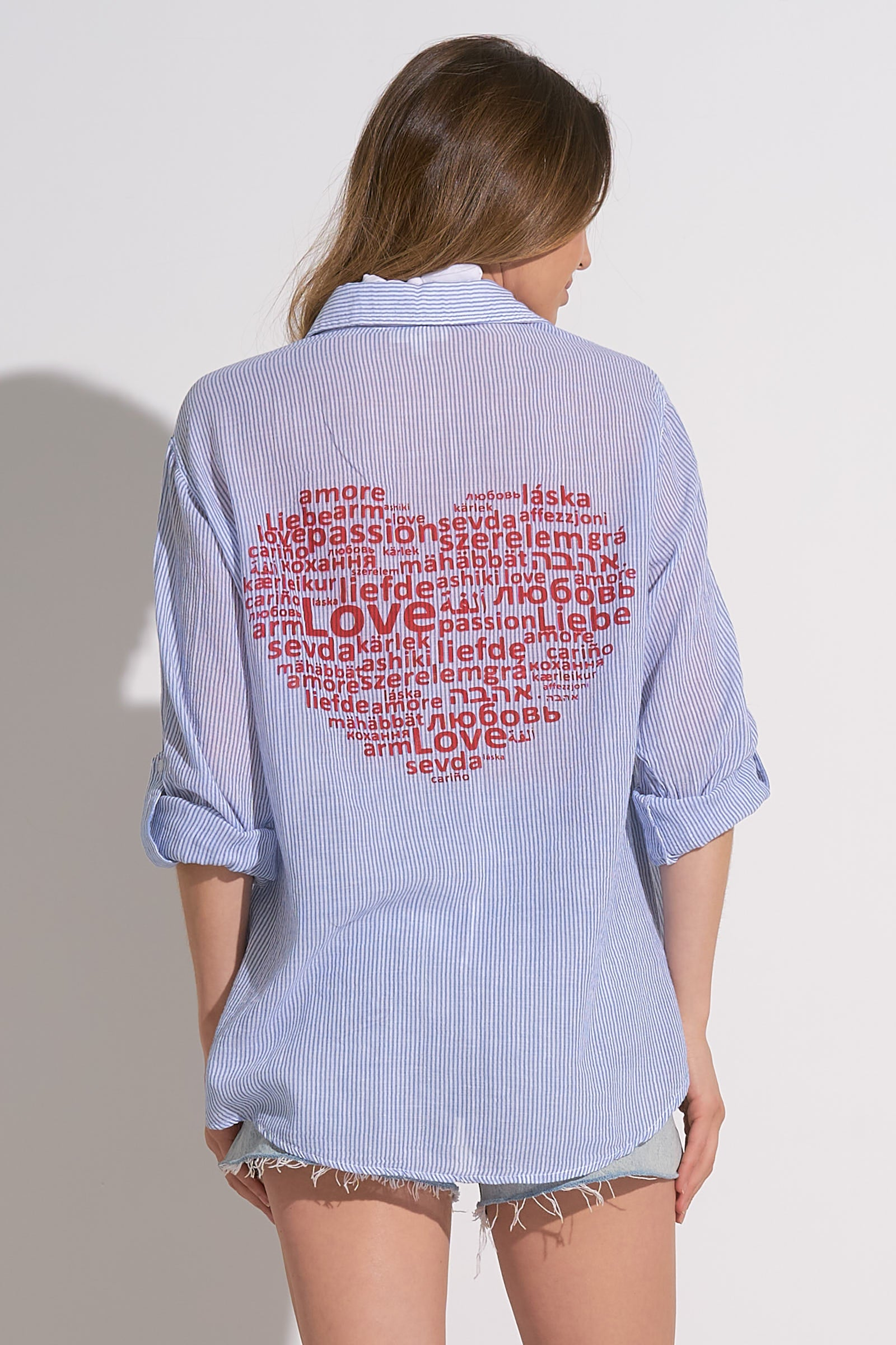 Model wearing a sheer blue and white striped button down top with a heart of the word love on back.