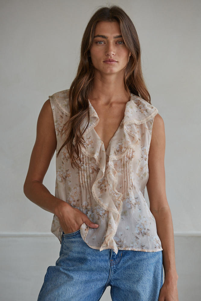 Woman wearing a sleeveless patterned top and blue jeans against a plain background