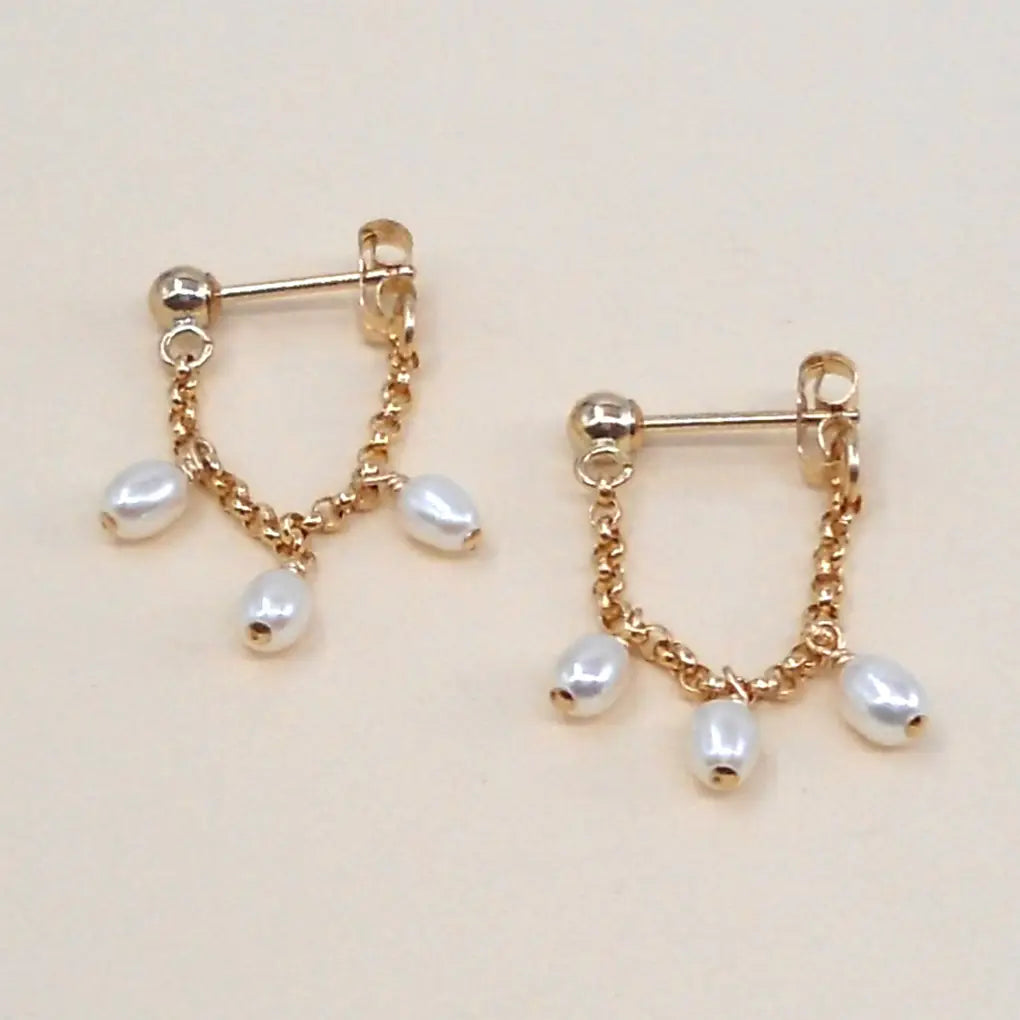 Gold earrings with pearl drops on a beige background