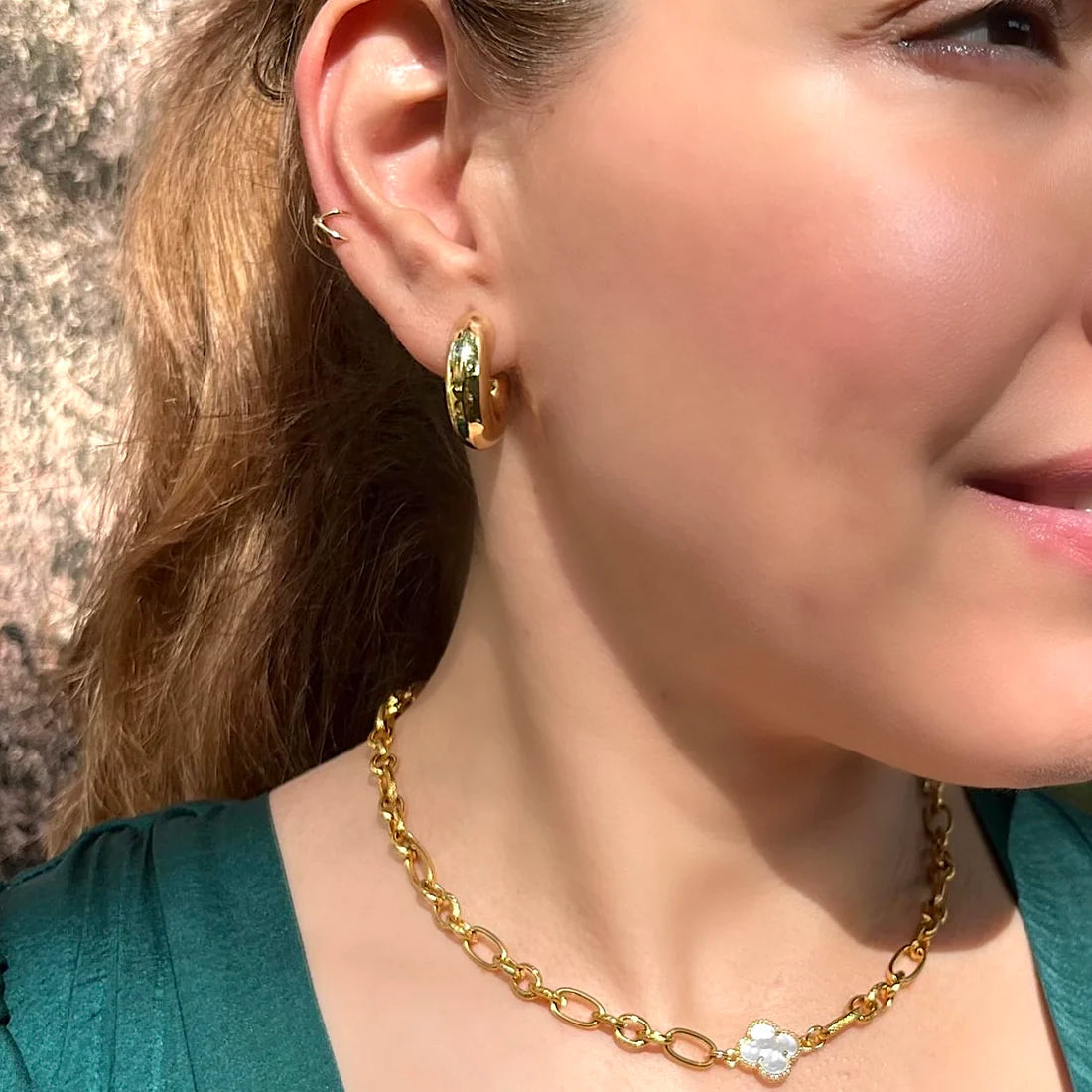 Close-up of a person wearing gold hoop earrings and a gold chain necklace.