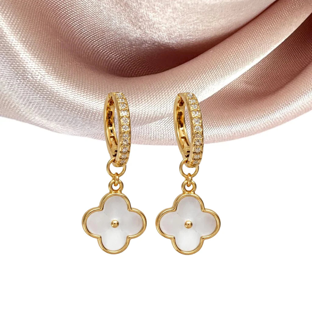 Gold hoop earrings with white floral charms on a pink satin background
